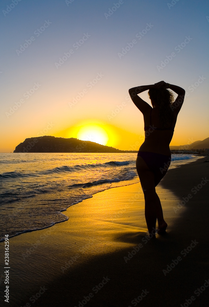 Silhouette of a slim woman on the seashore against the background of the sunset.