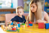 Cute female teacher and child toddler boy playing educational toys in kindergarten or nursery