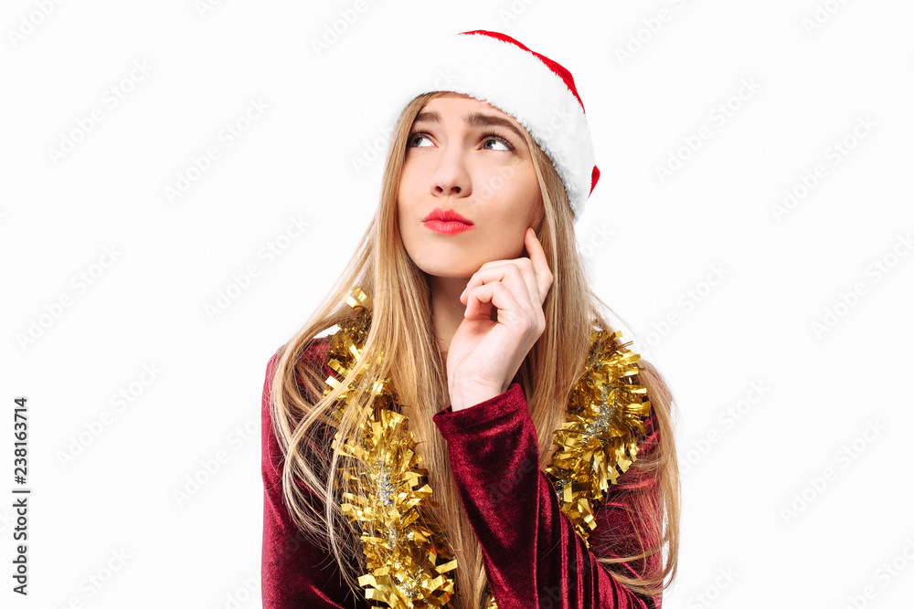 Beautiful cute girl in the hat of Santa Claus and in a dress, dreams and looks away.