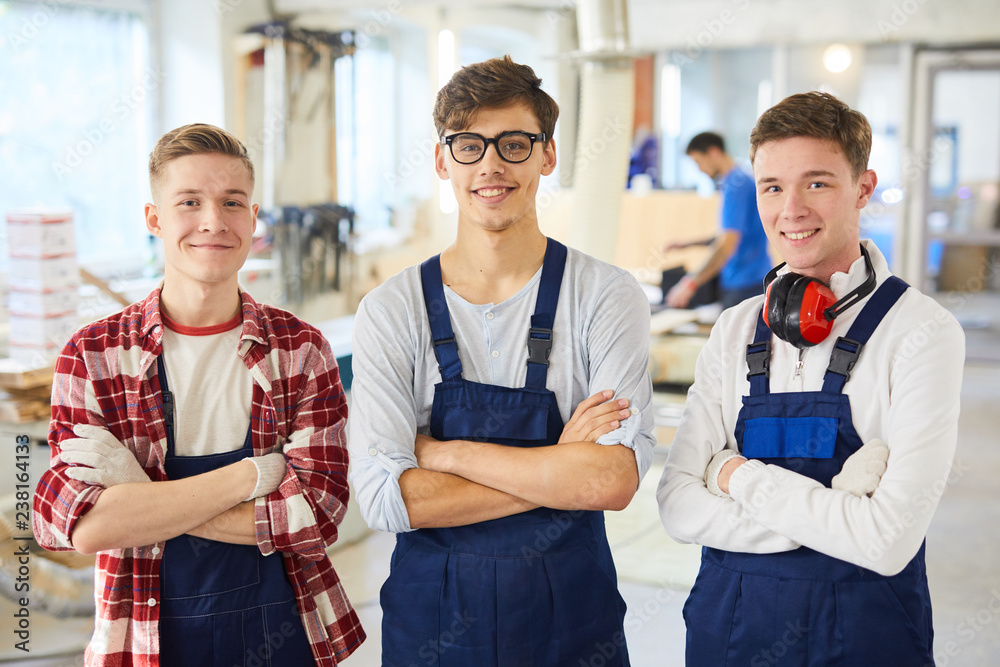 Naklejka premium Smiling confident young carpentry students in blue uniform standing in line and looming at camera in workshop