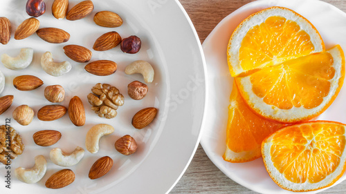Assorted Nuts, Orange Slices On White Plates On Wooden Table. Healthy Organic Snack, Breakfast, Food Ingredients. Flat Lay Top-Down Composition.