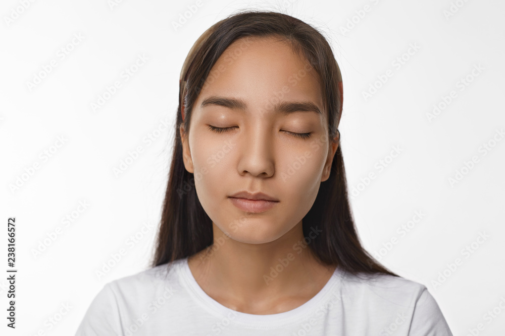 Peace, calmness, harmony and meditation concept. Beautiful young Asian woman with loose black hair having peaceful serene facial expression while meditating in studio, keeping her eyes closed Peace, calmness, harmony and meditation concept. Beautiful young Asian woman with loose black hair having peaceful serene facial expression while meditating in studio, keeping her eyes closed