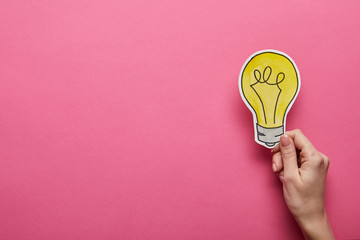 top view of hand holding yellow light bulb on pink background