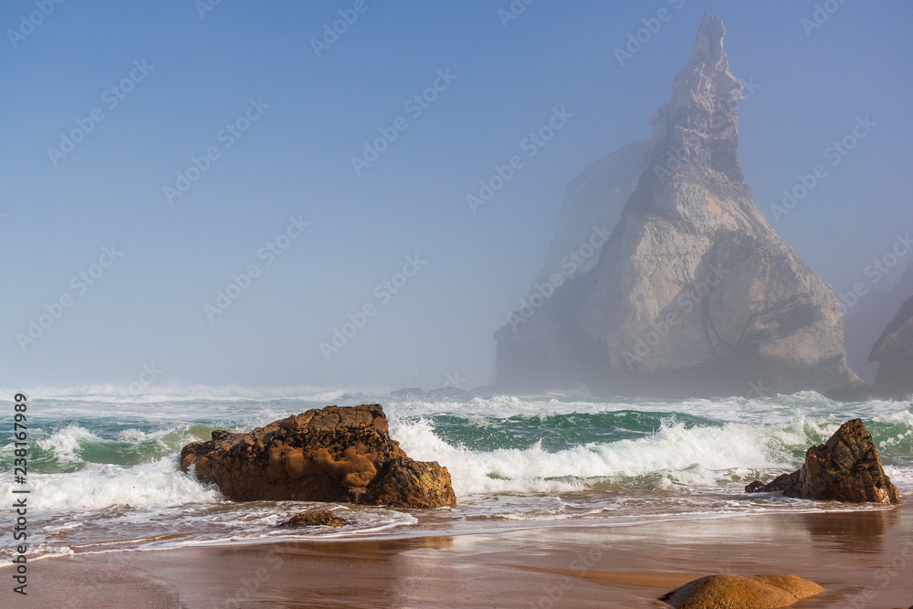 Dreamy landscape of Ursa beach, Praia Da Ursa, Sintra, Portugal, on a foggy summer morning with  ocean waves crashing on rocks.
