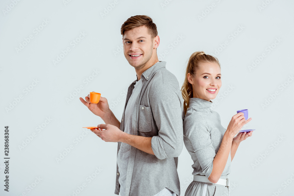 smiling couple in grey clothing drinking coffee and looking at camera isolated on grey