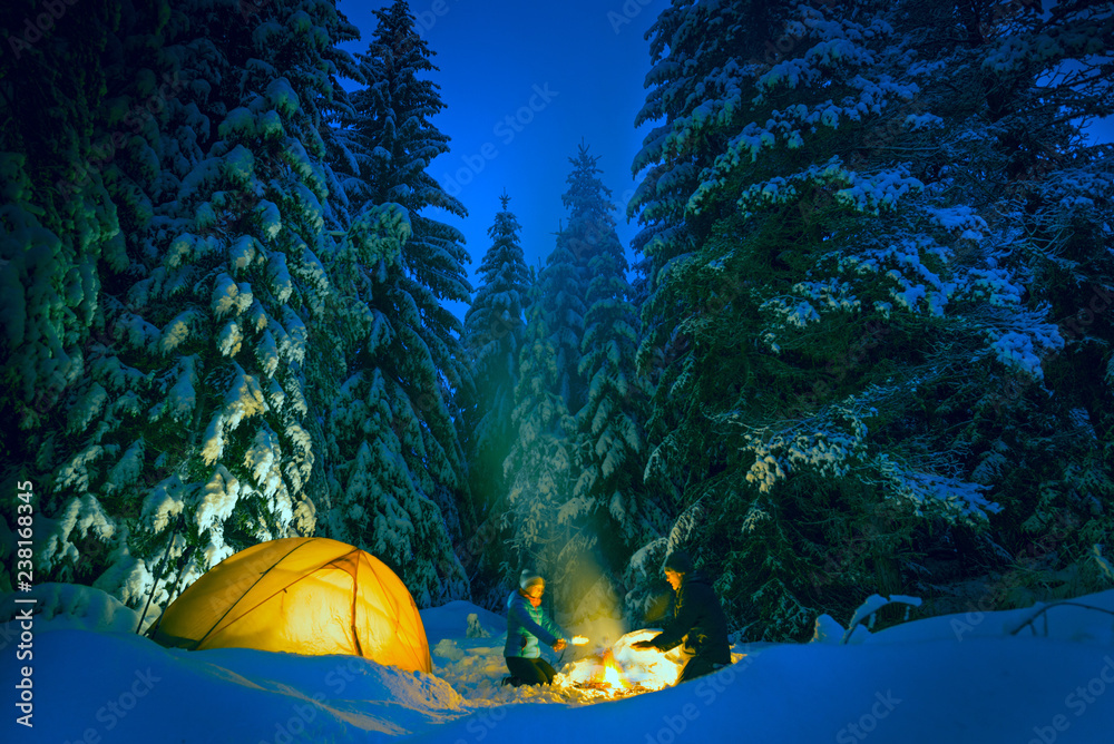 couple camping with campfire and tent outdoors in winter - obrazy, fototapety, plakaty 