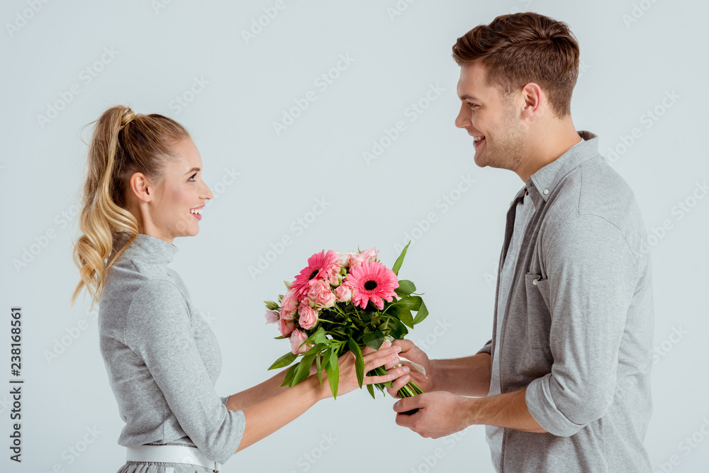 man giving pink flower bouquet to beautiful woman isolated on grey