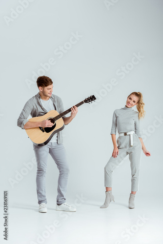 man playing acoustic guitar while smiling woman dancing on grey background © LIGHTFIELD STUDIOS