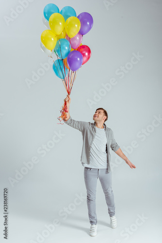 happy man in grey clothing holding bundle of colorful balloons on grey background © LIGHTFIELD STUDIOS