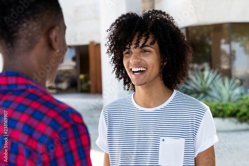 Young adult man with long hair talking with african friend