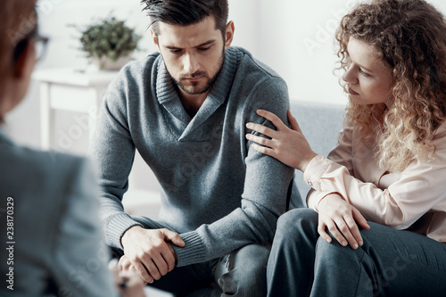 Fototapeta Naklejka Na Ścianę i Meble -  Supportive beautiful wife touching husband's arm during psychotherapy session for married couples with problems