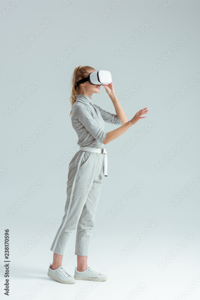girl in grey clothing and vr headset gesturing while having virtual reality experience on grey background girl in grey clothing and vr headset gesturing while having virtual reality experience on grey background