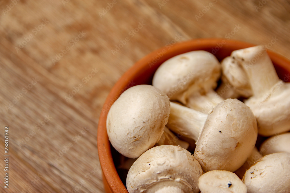 Fresh white champignon mushrooms in brown ceramic bowl on wooden vintage table