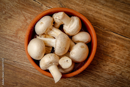 Fresh white champignon mushrooms in brown ceramic bowl on wooden vintage table