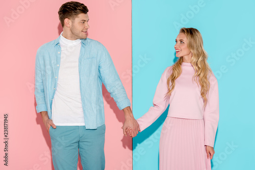happy couple holding hands and looking at each other on pink and blue background
