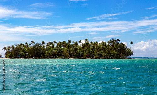 Landscape of little island with palm trees, seen from the water surface in the lagoon, Pacific ocean, French Polynesia