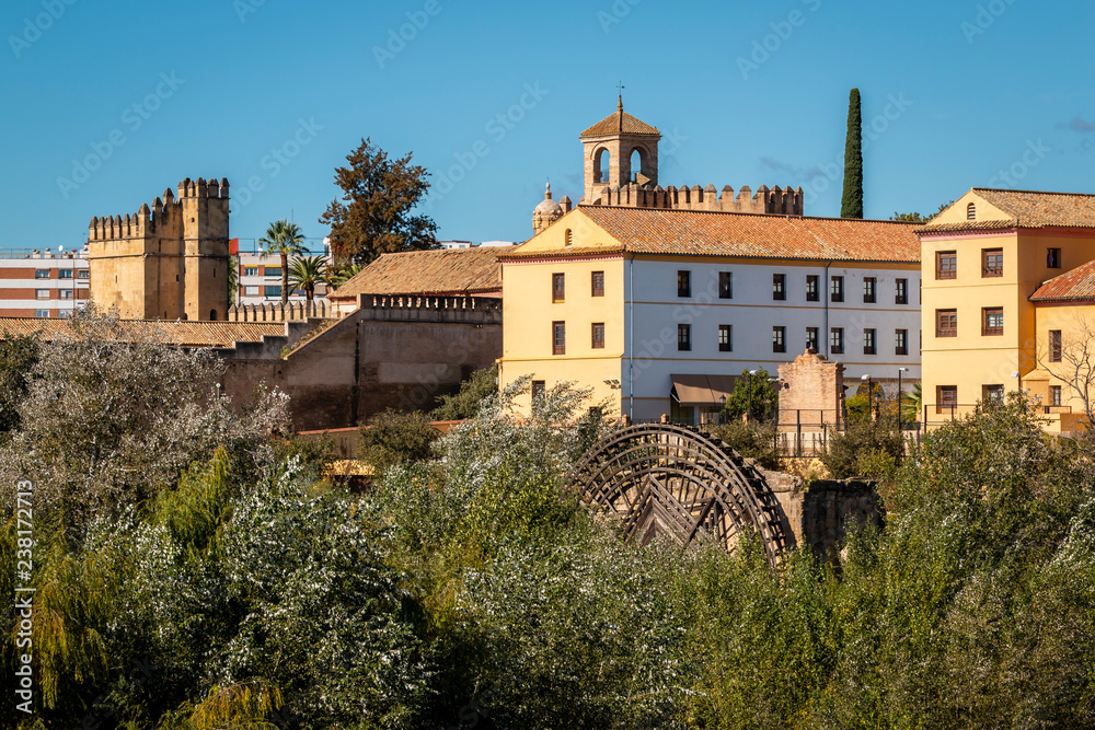 Exterior of old architectural buildings with millstone in green vegetation against blue sky in Cordoba, Spain