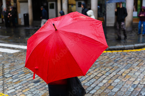 person with red rain umbrella crosses a city street