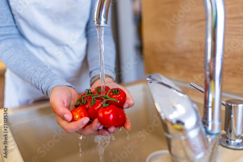 Hands woman washing vegetables - tomatoes. Preparation of fresh salad. Fresh vegetables on the worktop near to sink in a modern kitchen interior, healthy food concept. Selective focus.