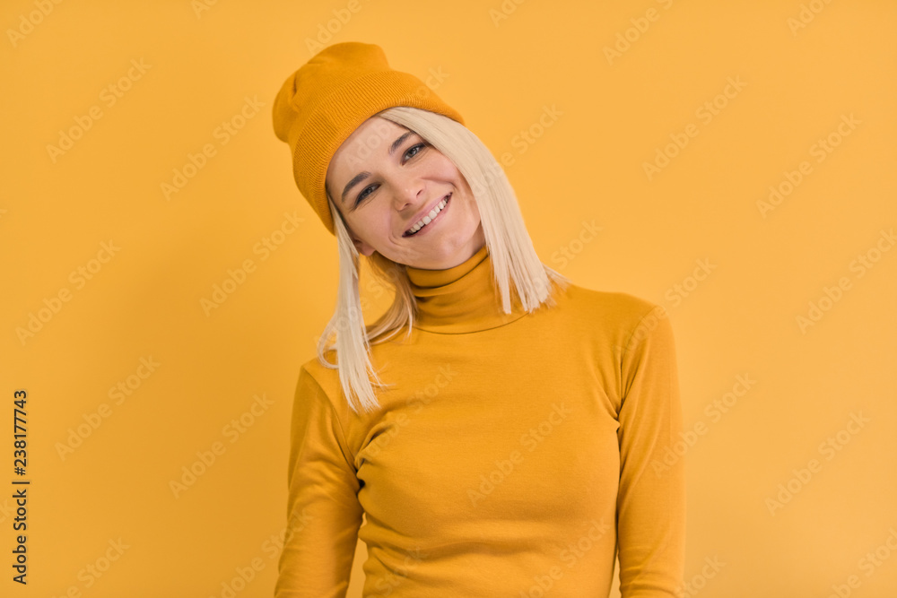 Monochrome studio portrait of happy Caucasian woman with positive smile, has blonde hair, looking to the camera, isolated on yellow wall. People and emotions concept