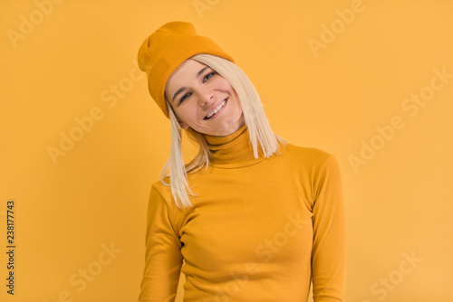Monochrome studio portrait of happy Caucasian woman with positive smile, has blonde hair, looking to the camera, isolated on yellow wall. People and emotions concept