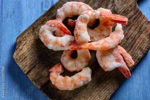 Boiled frozen shrimps are on old wooden board on blue wooden background