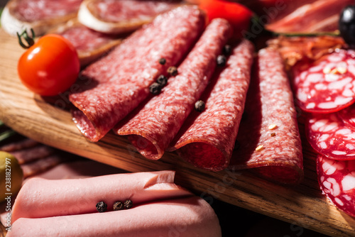 close up view of wooden cutting board with delicious sliced salami, spices and vegetables