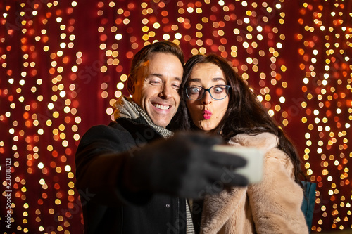 Two friends taking selfie in front of light wall at Christmas market.