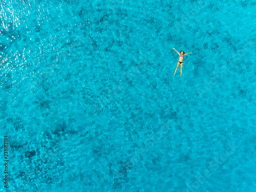 Aerial view of pregnant woman floating on her back in transparent sea.