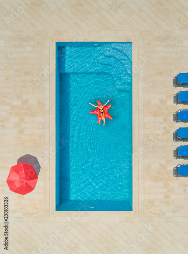 Aerial view of woman on star shapes inflatable mattress in swimming pool.