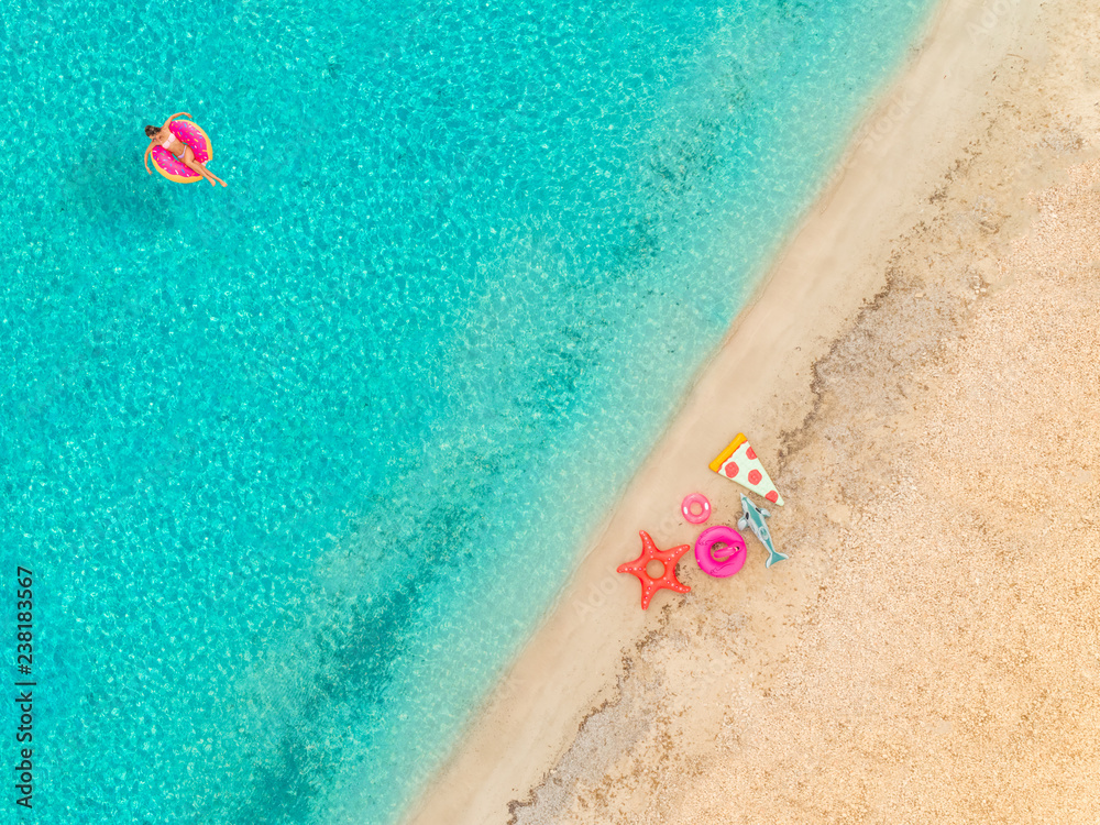 Aerial view of woman floating on inflatable mattress by sandy beach.