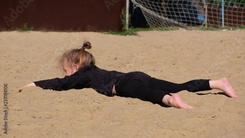 Little funny girl in a black suit swims in the sand imaging the sea or pool