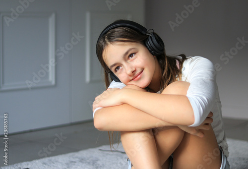 Photos Beautiful happy romantic smiling preteen girl with wireless headphones listening to music sitting on floor at home hugging her khees relaxing