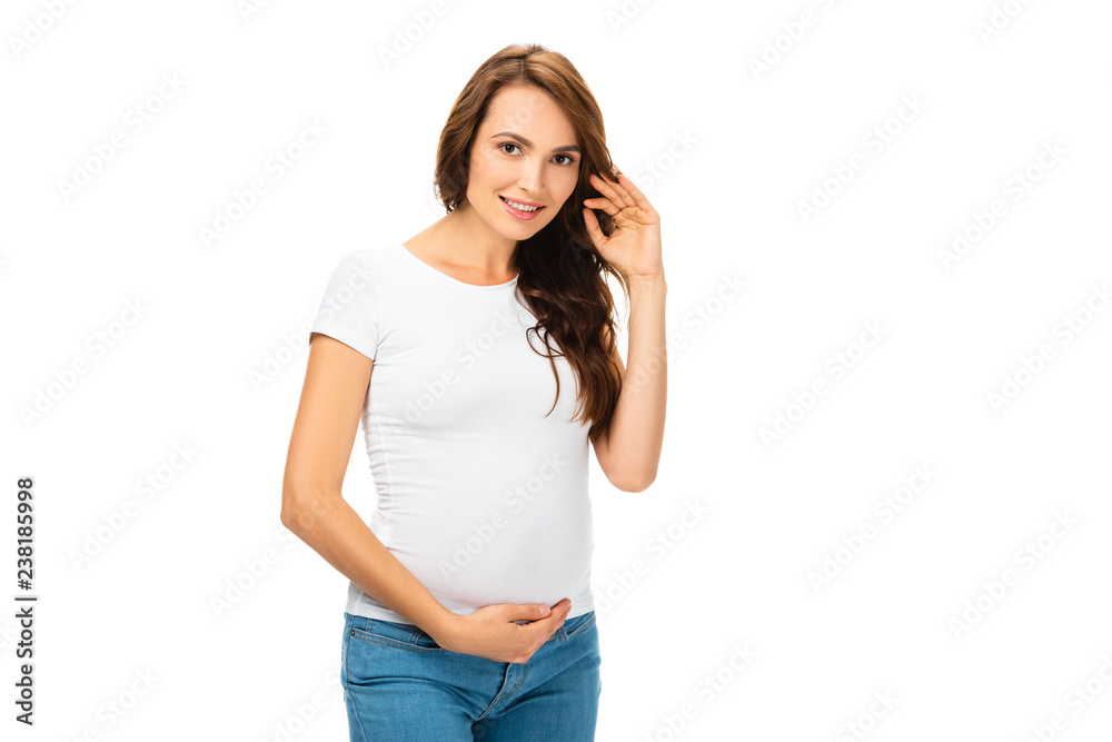 beautiful pregnant woman touching hair with left hand and looking at camera isolated on white