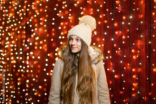 Teenager with long hair posing in front of lights wall at Christmas market.