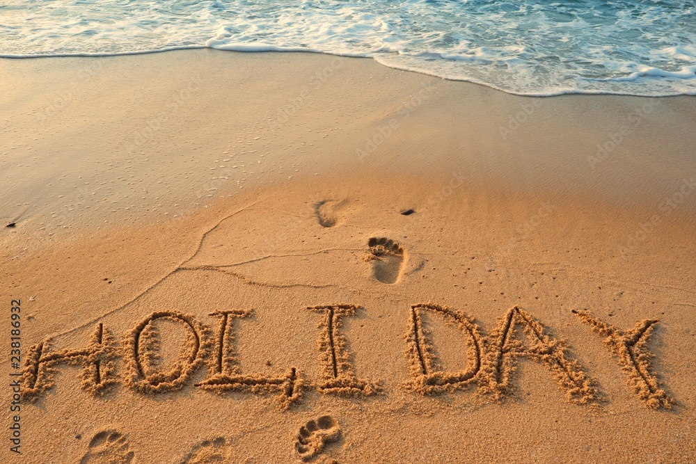 Fototapeta premium Concept HOLIDAY handwriting on sand beach with waves and blue ocean.