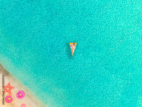 Aerial view of woman floating on inflatable mattress by sandy beach.