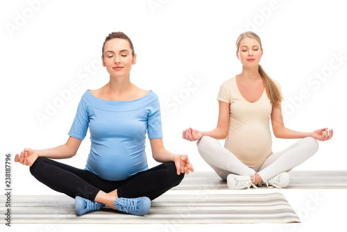 two pregnant women sitting on floor and meditating isolated on white