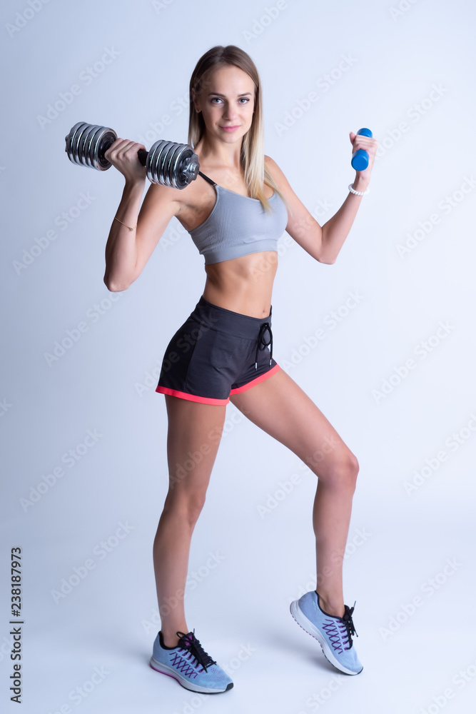 Beautiful young slim girl with dumbbells on a white background. Novice athlete Beautiful young slim girl with dumbbells on a white background. Novice athlete