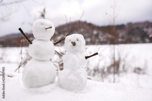 Two real tiny, little snowman in nature in snowy, cold day in mountains. Concept of beautiful winter and kids or family having fun on holidays. Merry Christmas. 