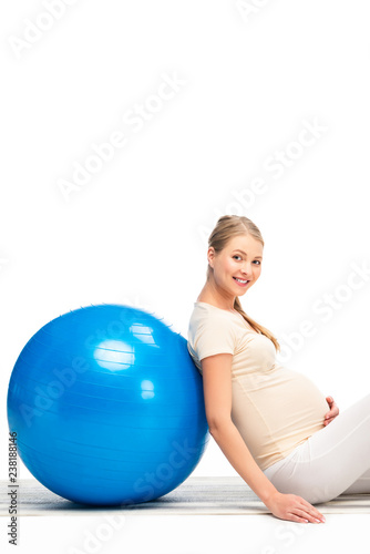 pregnant blonde woman leaning on blue fitness ball isolated on white