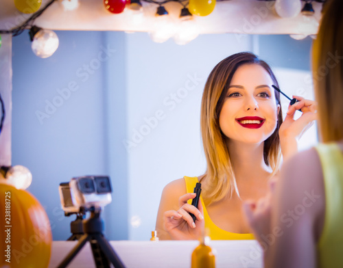 Young caucasian blogger woman applying cosmetics at camera for Video-sharing website. Home location near a mirror