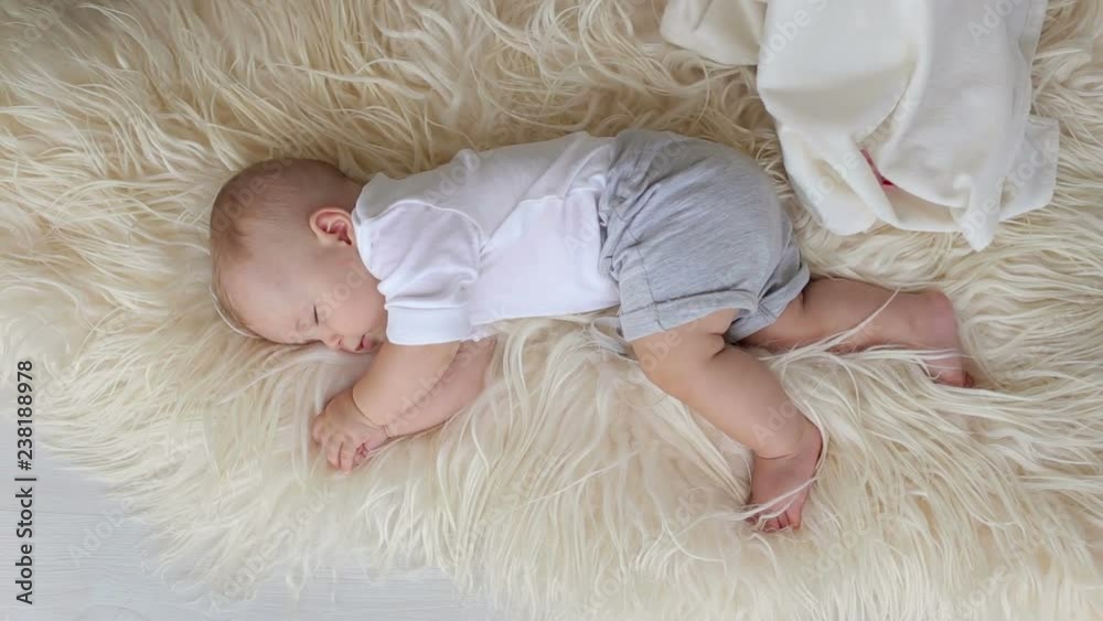 Close-up of a little newborn boy sleeping on a fluffy blanket at home in the bedroom, caring mother gently covers the child with a blanket. Close-up of a little newborn boy sleeping on a fluffy blanket at home in the bedroom, caring mother gently covers the child with a blanket.