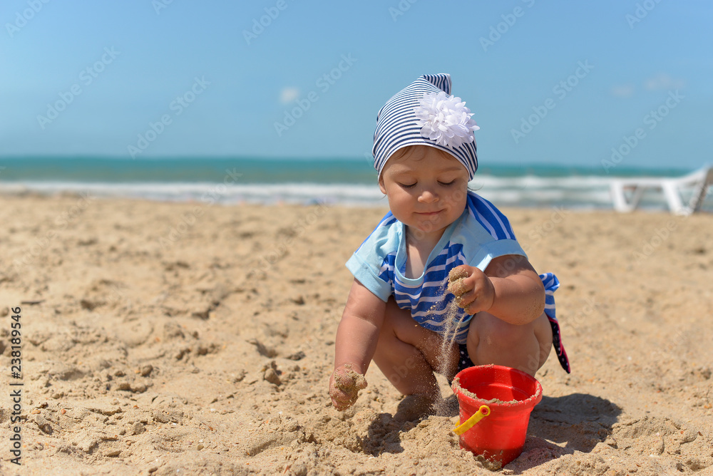 A little girl in a scarf playing on the sandy beach in the summer. A little girl in a scarf playing on the sandy beach in the summer.