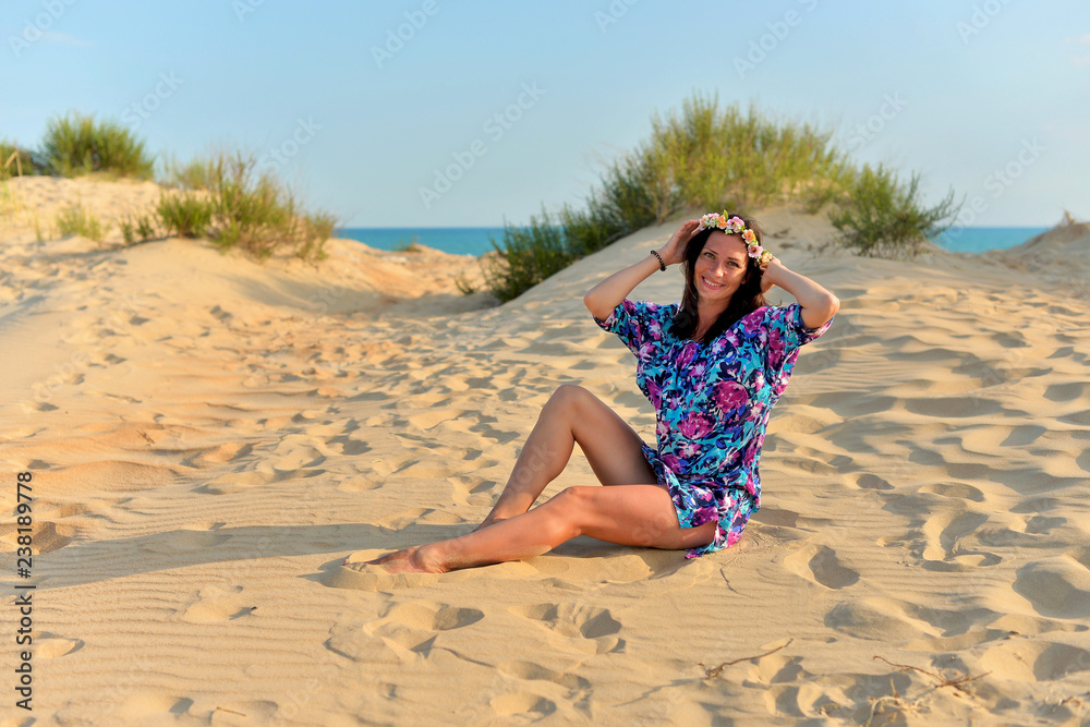 A young woman with a wreath of flowers on her head resting on a sandy beach on a warm evening
