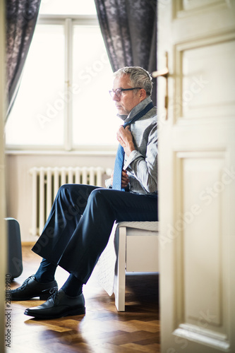 Mature businessman on a business trip in a hotel room, getting dressed.