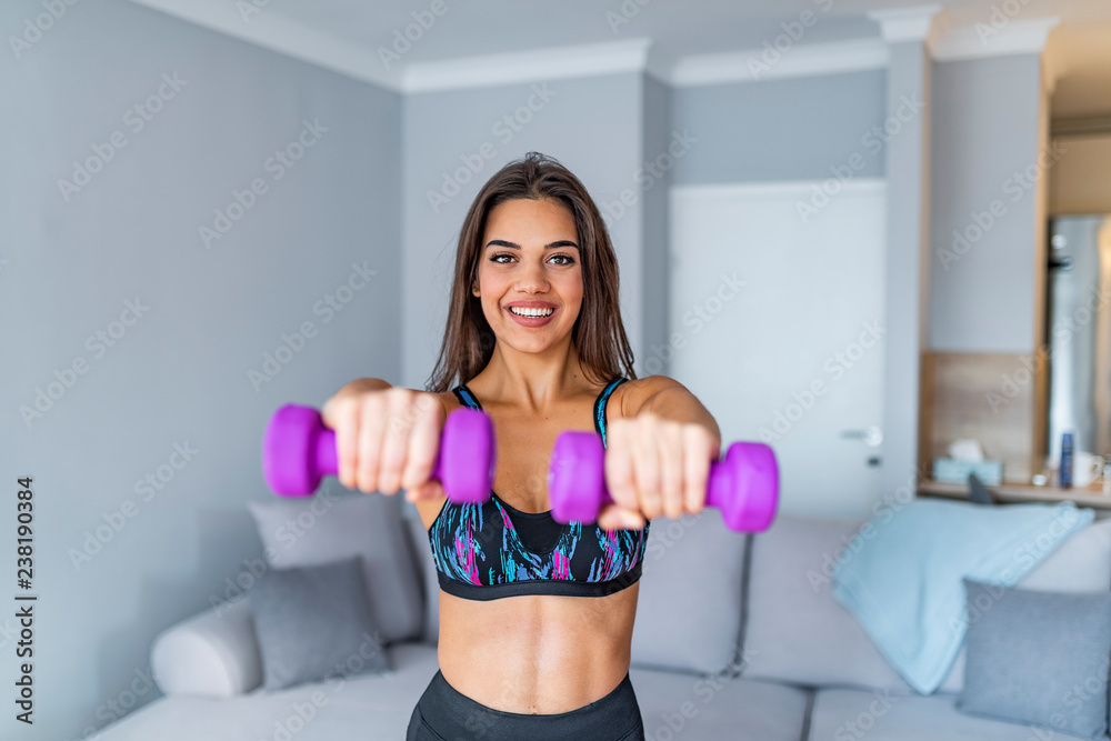 Determined woman losing weight at home and exercising with dumbbells Determined woman losing weight at home and exercising with dumbbells
