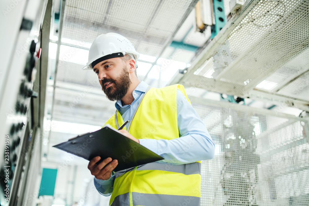 A portrait of an industrial man engineer with clipboard in a factory, working. A portrait of an industrial man engineer with clipboard in a factory, working.