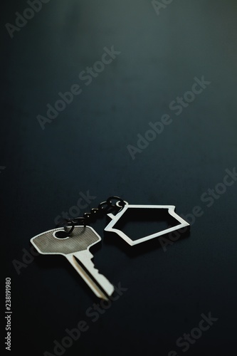 Home key with house keyring on black wood table in dark tone, real estate concept