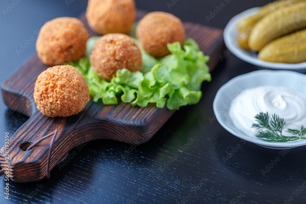 Falafel lies on a wooden cutting board. On the table lie tomatoes, cucumbers, lettuce, dill, lemon, sour cream. Falafel lies on a wooden cutting board. On the table lie tomatoes, cucumbers, lettuce, dill, lemon, sour cream.